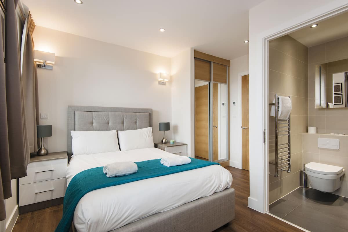 A modern hotel room with a large bed, bedside tables with lamps, a bathroom with a toilet and shower, and a sliding door closet.