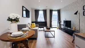 Una sala de estar moderna con sofá, mesa de centro, comedor para dos personas y televisor sobre un mueble.