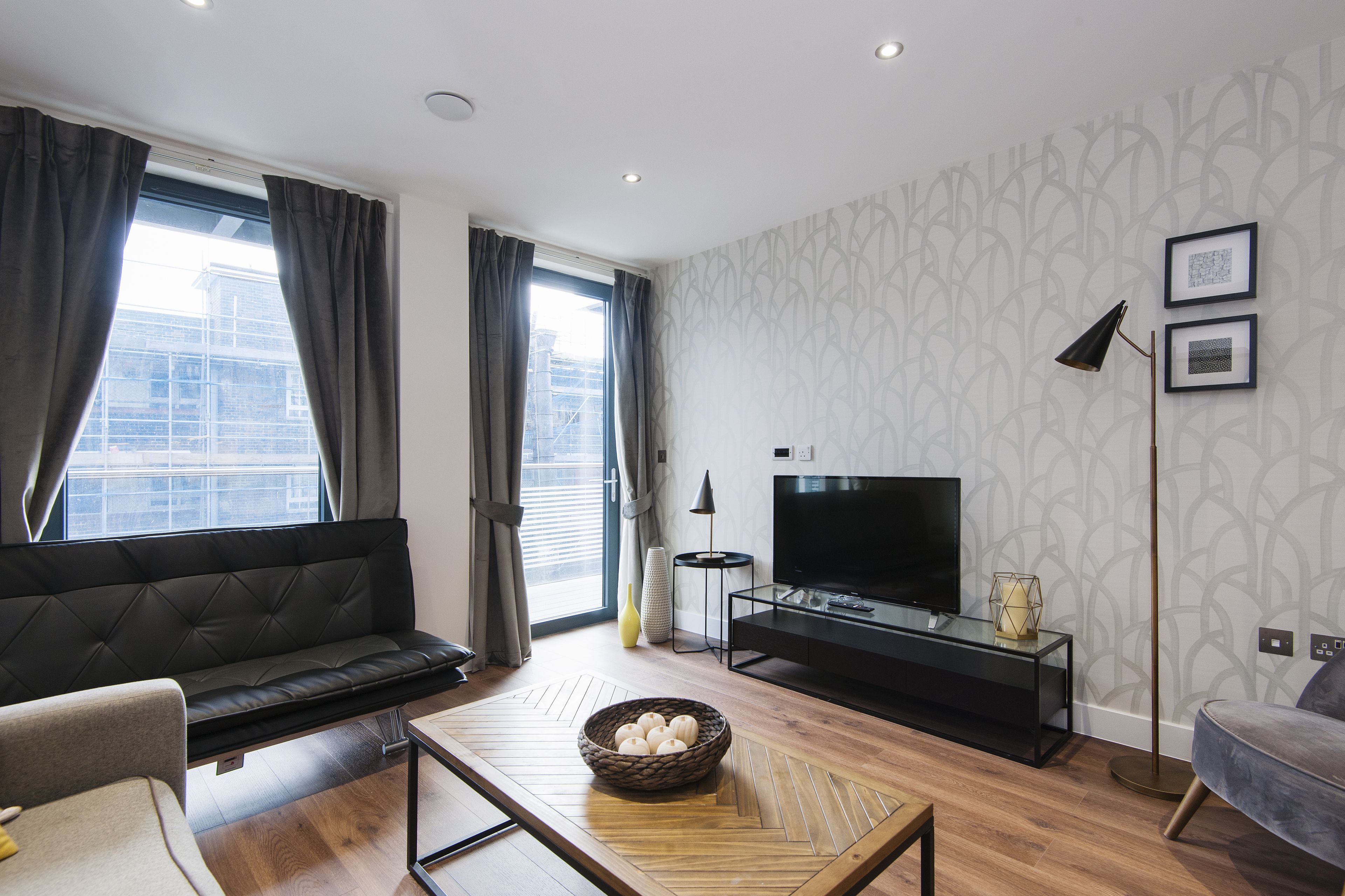 A modern living room with a sofa, a coffee table, a TV, and a patterned wall.