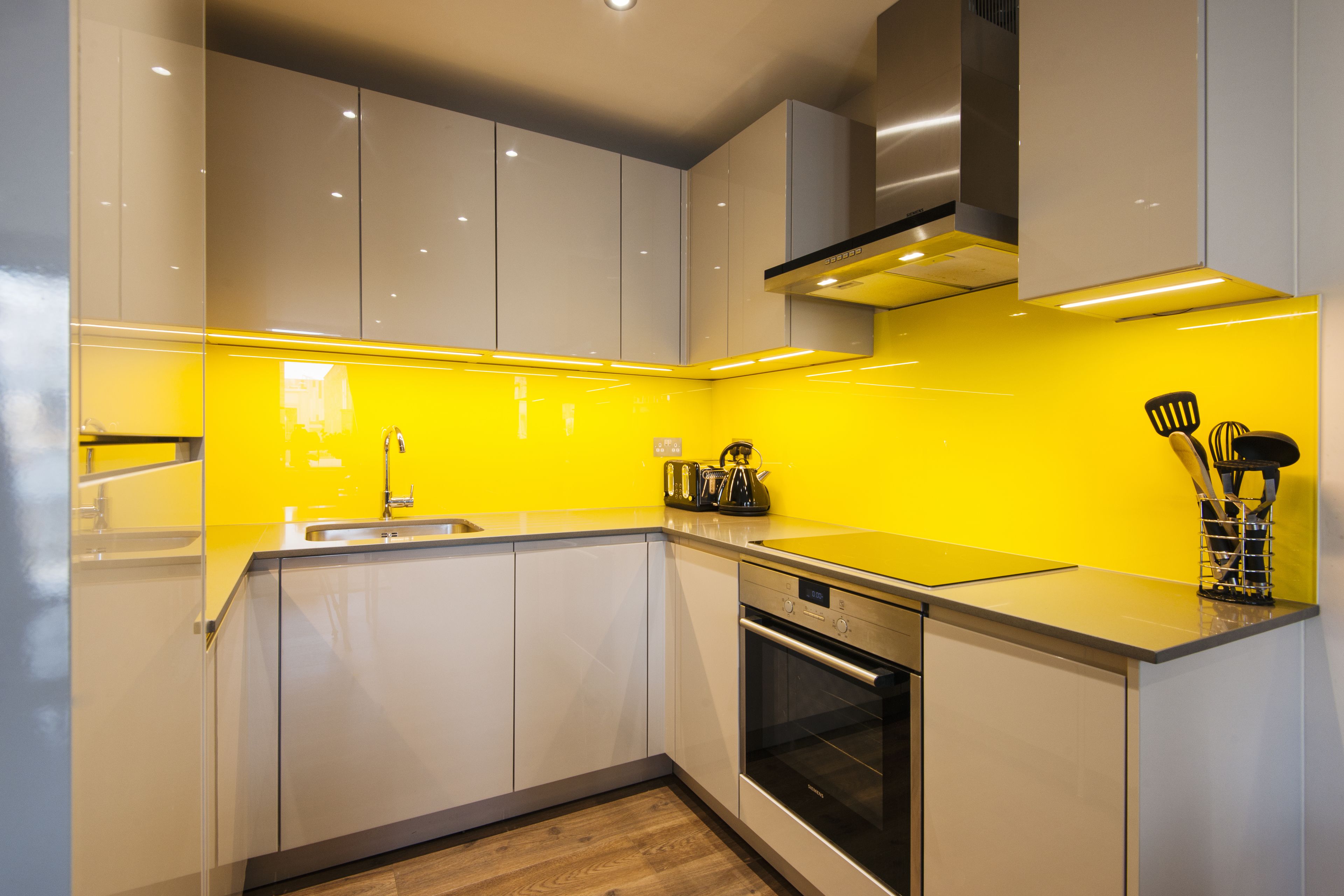 A modern kitchen with white cabinets, a stainless steel oven, and a yellow backsplash.