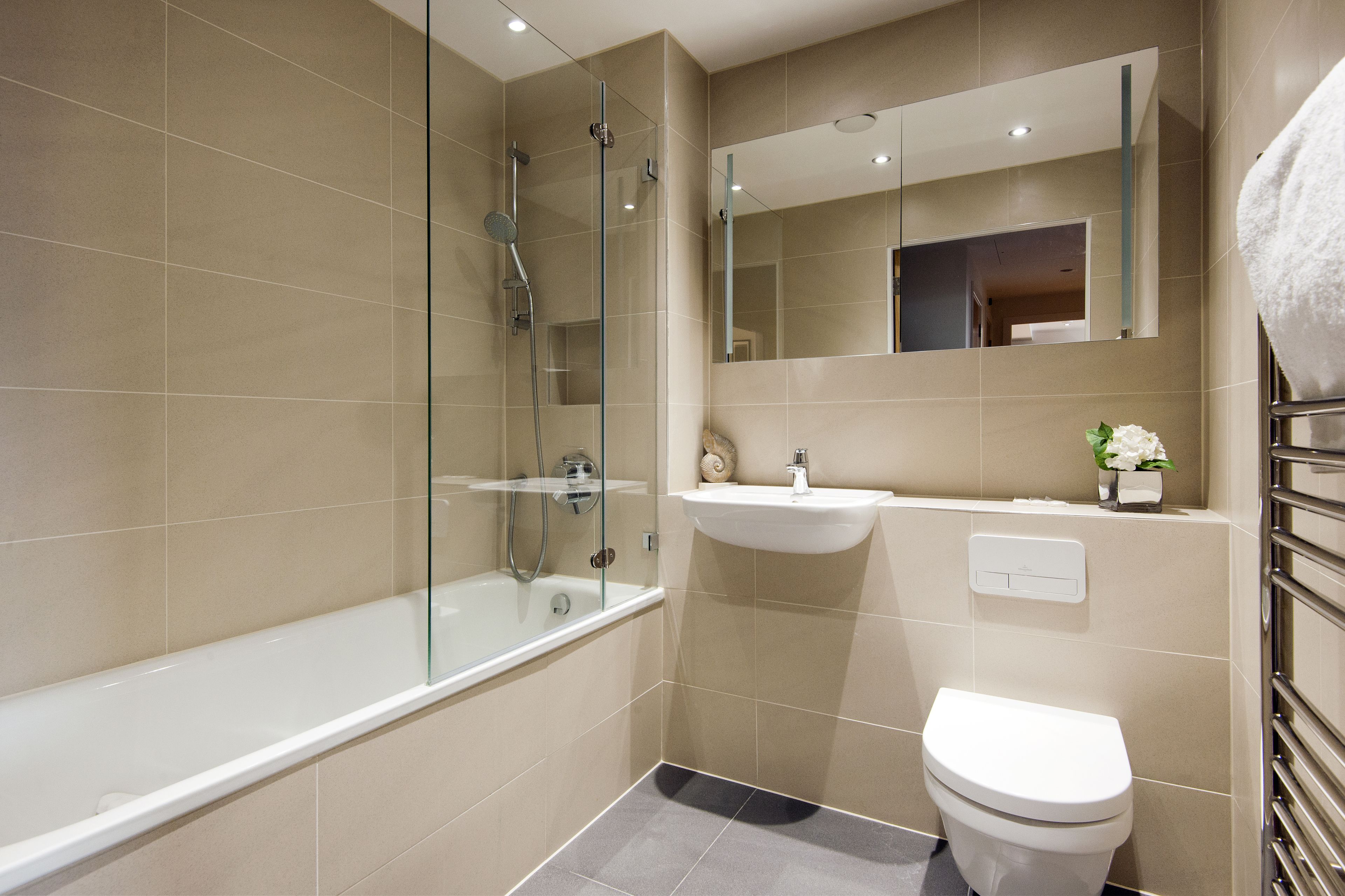 A modern bathroom with a glass-enclosed shower, a white bathtub, a sink, and a toilet.