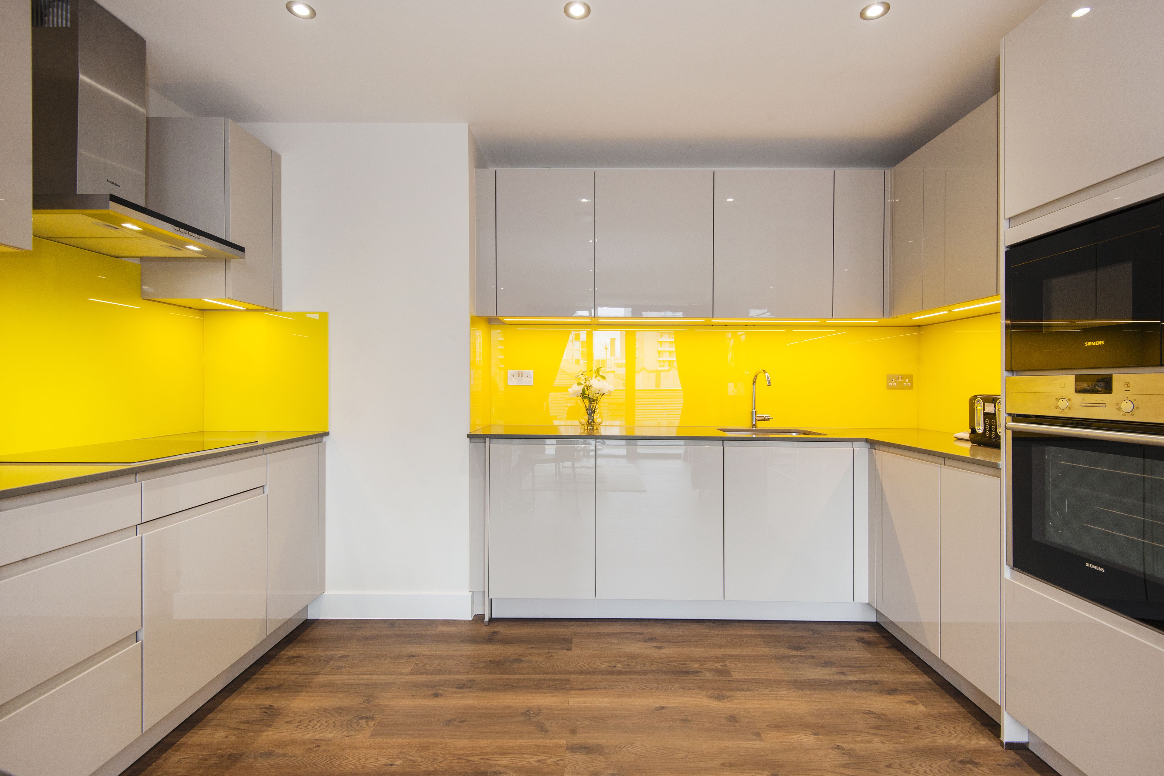 A modern kitchen with white cabinets, a yellow backsplash, and a wooden floor.