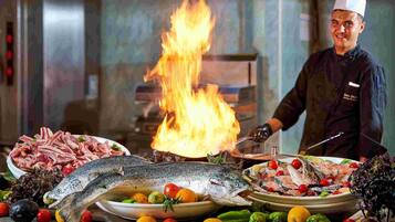 A chef cooking with a large fish on a grill, surrounded by various vegetables and meats.