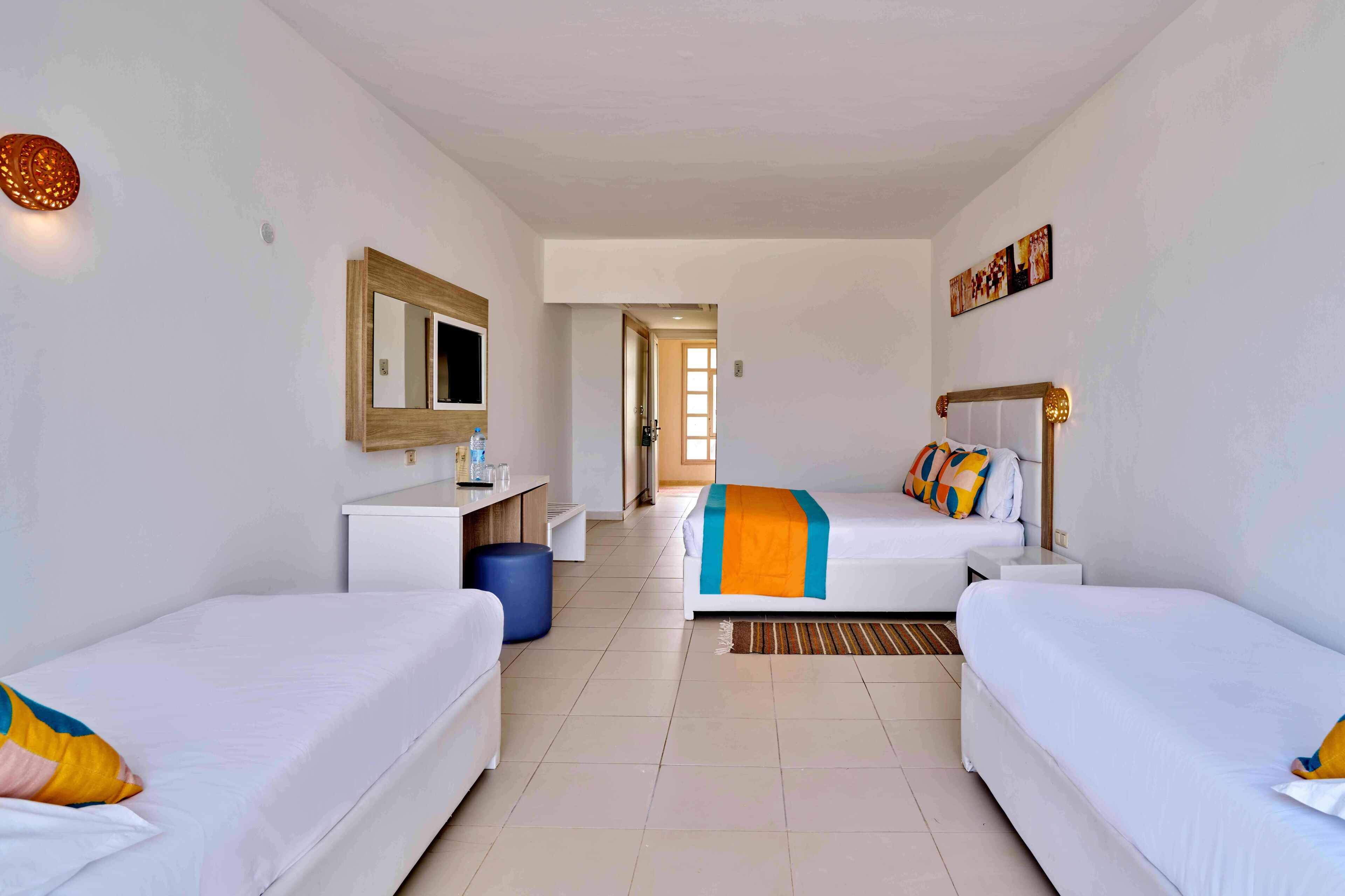 A hotel room with two single beds, a desk, a chair, a mirror, and a large window.