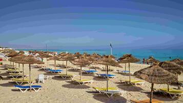 Een strand met rijen ligbedden en rieten parasols.