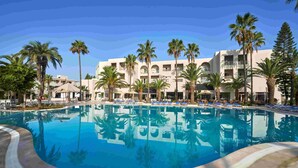Une piscine entourée de palmiers et un bâtiment d’hôtel doté de nombreux balcons.