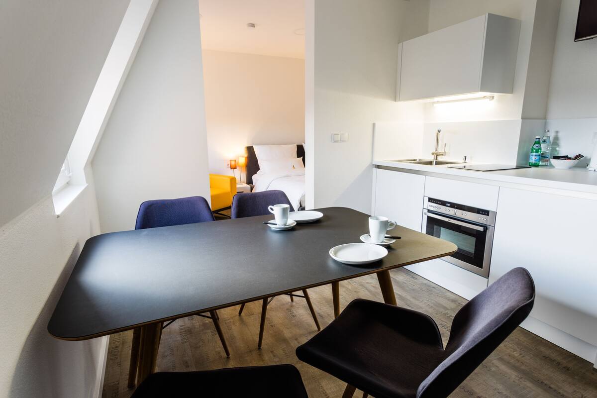 Een moderne hotelkamer met een zithoek, kitchenette en een bed met nachtkastje.