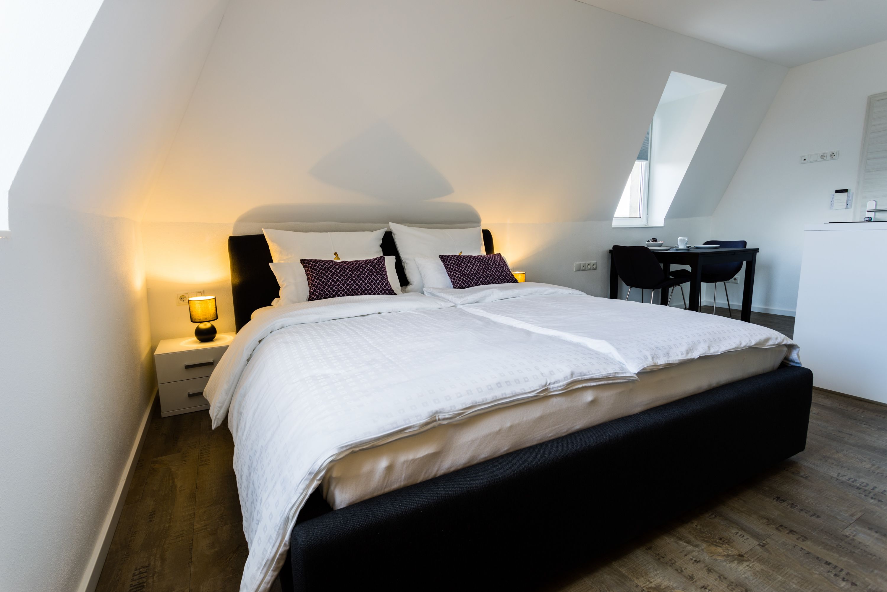 A modern bedroom with a large bed, a desk, and a chair.