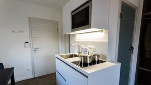 Een compacte keuken met een ingebouwde magnetron, een spoelbak met kraan en een kookplaat met pannen.