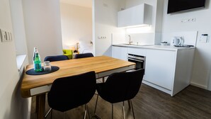 Een kleine keuken met een houten tafel, zwarte stoelen, een wit aanrecht en een inbouwoven.