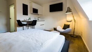 Een moderne hotelkamer met een groot bed, een bureau met twee stoelen, een flatscreen televisie en een vloerlamp.