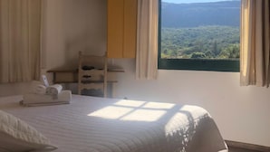 Ein Schlafzimmer mit einem Bett, einem an der Wand montierten Fernseher, einem Fenster mit Blick auf Grünflächen und einem Holzschrank.