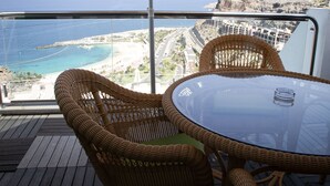 Een rieten stoel en tafeltje op een balkon met uitzicht op zee en een strand.