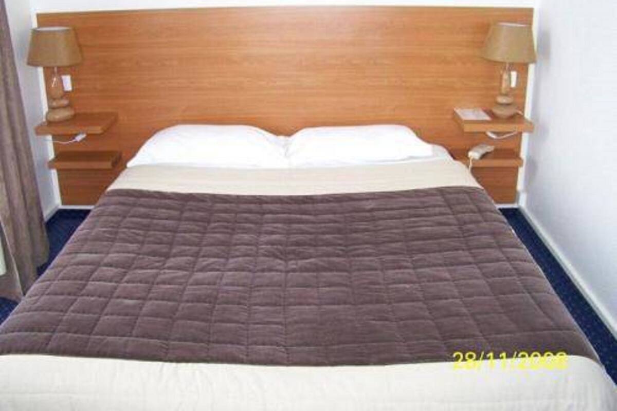 Ein Hotelzimmer mit einem hölzernen Kopfteil, einer braunen gesteppten Bettdecke, weißen Kissen und zwei Nachttischlampen.