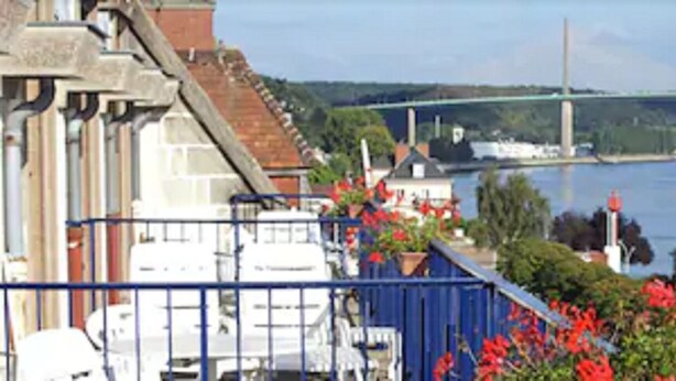 A riverside view with a bridge, buildings, and a blue fence with flowers. - Normotel - La Marine (Rives-en-Seine)