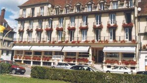 A multi-story hotel with a traditional European architectural style, featuring balconies with flower boxes, a central entrance, and a parking area in front. - Normotel - La Marine (Rives-en-Seine)