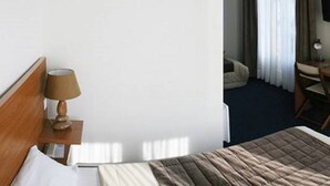 A hotel room with a bed, a bedside table with a lamp, a desk with a chair, and a television on the wall. - Normotel - La Marine (Rives-en-Seine)