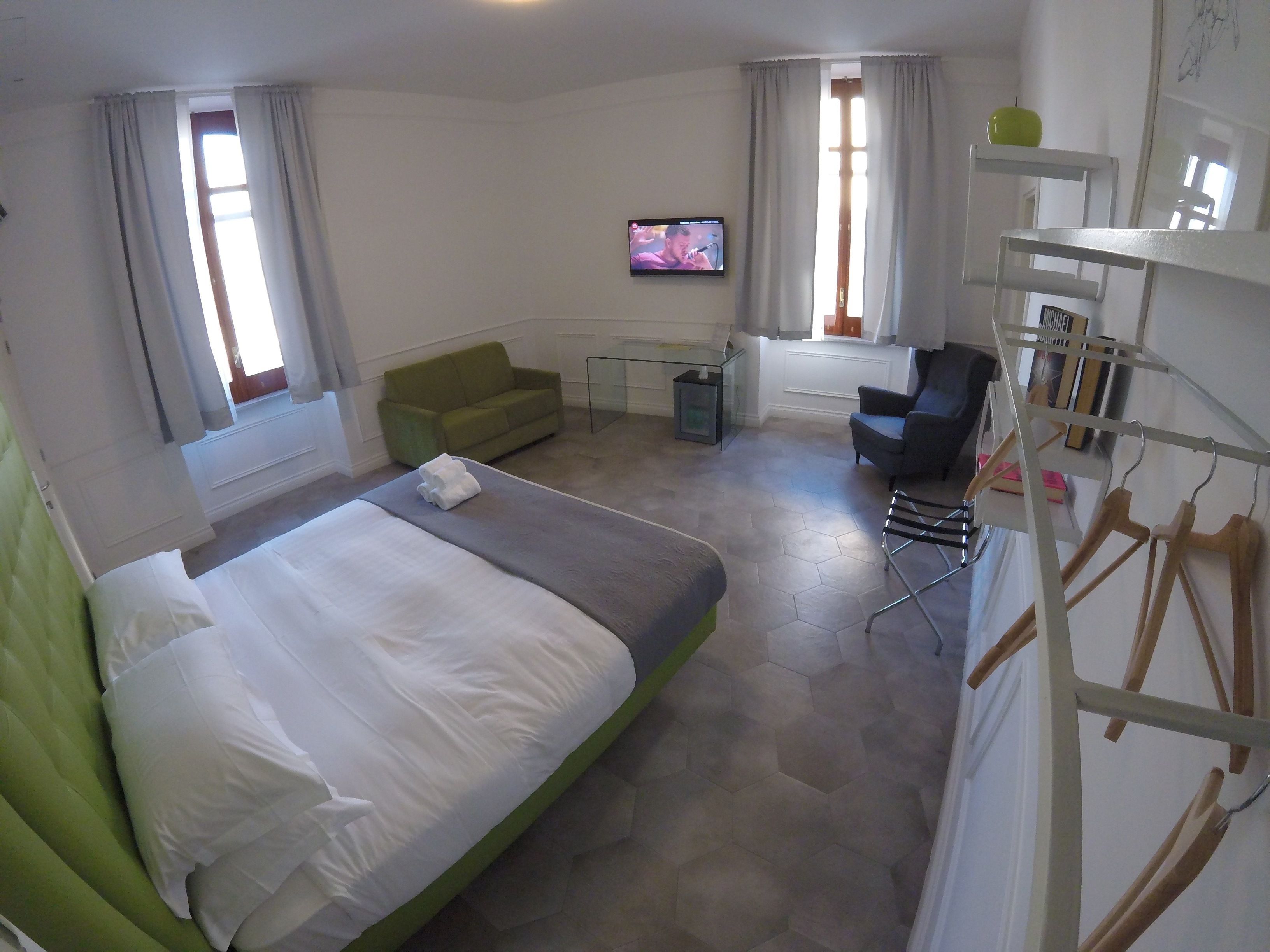 A hotel room with a bed, a green sofa, a desk with a computer, a chair, and a TV on the wall.