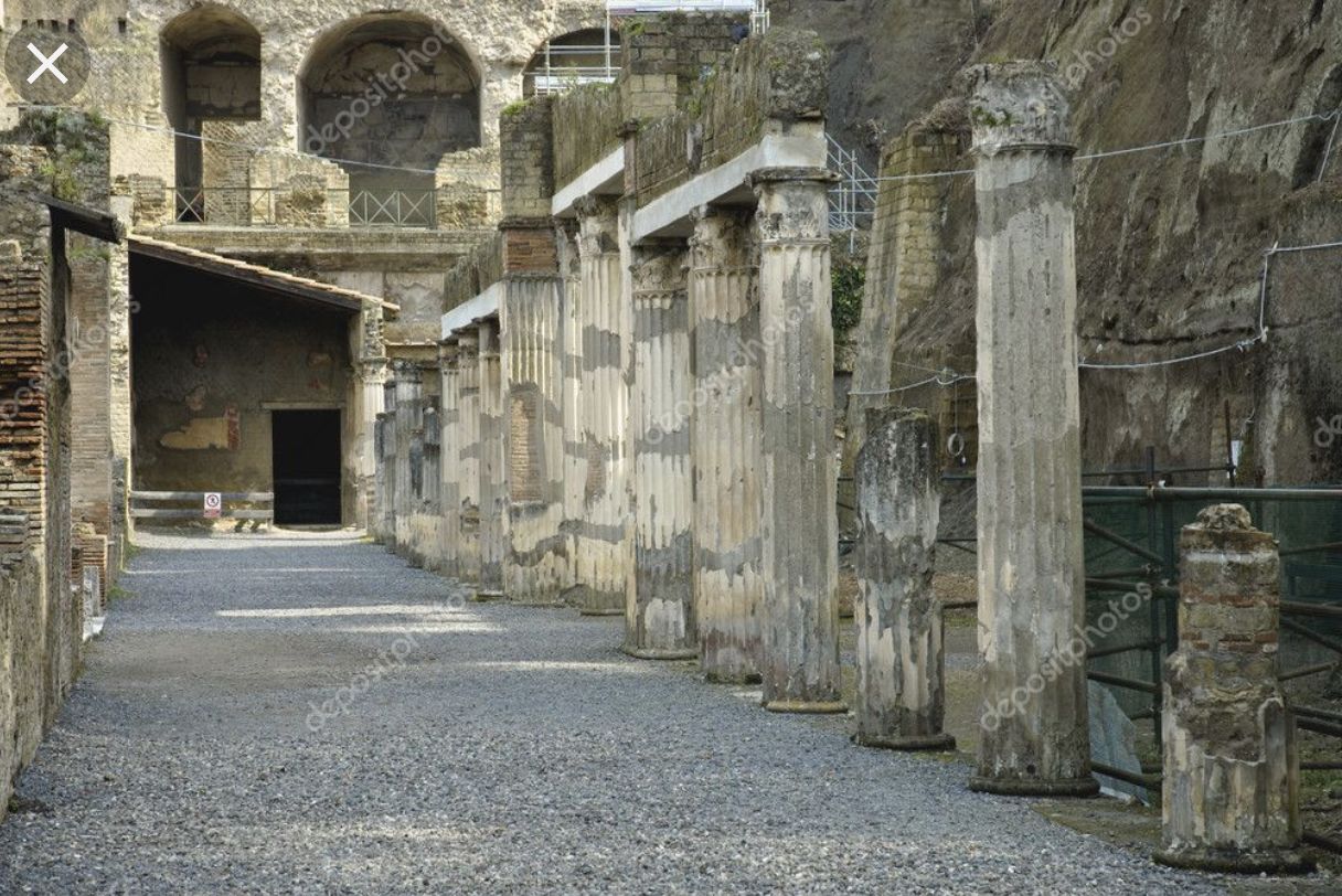 Un antiguo corredor de piedra con columnas y arcos, que conduce a un oscuro vano.