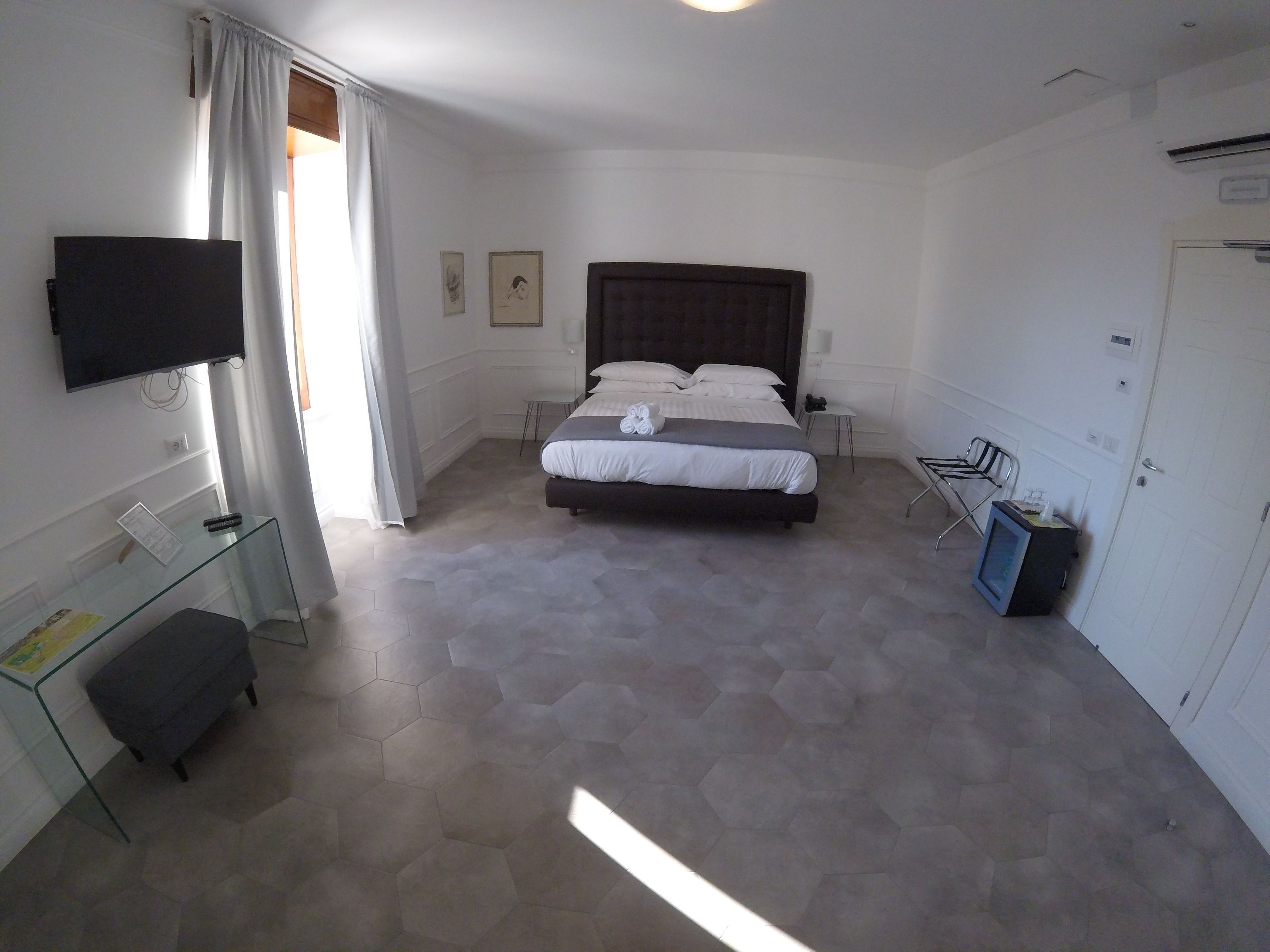 A hotel room with a large bed, a desk with a flat-screen TV, a chair, and a wardrobe.