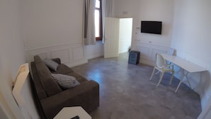 Een moderne woonkamer met een bank, een bijzettafeltje en een aan de muur bevestigde televisie.