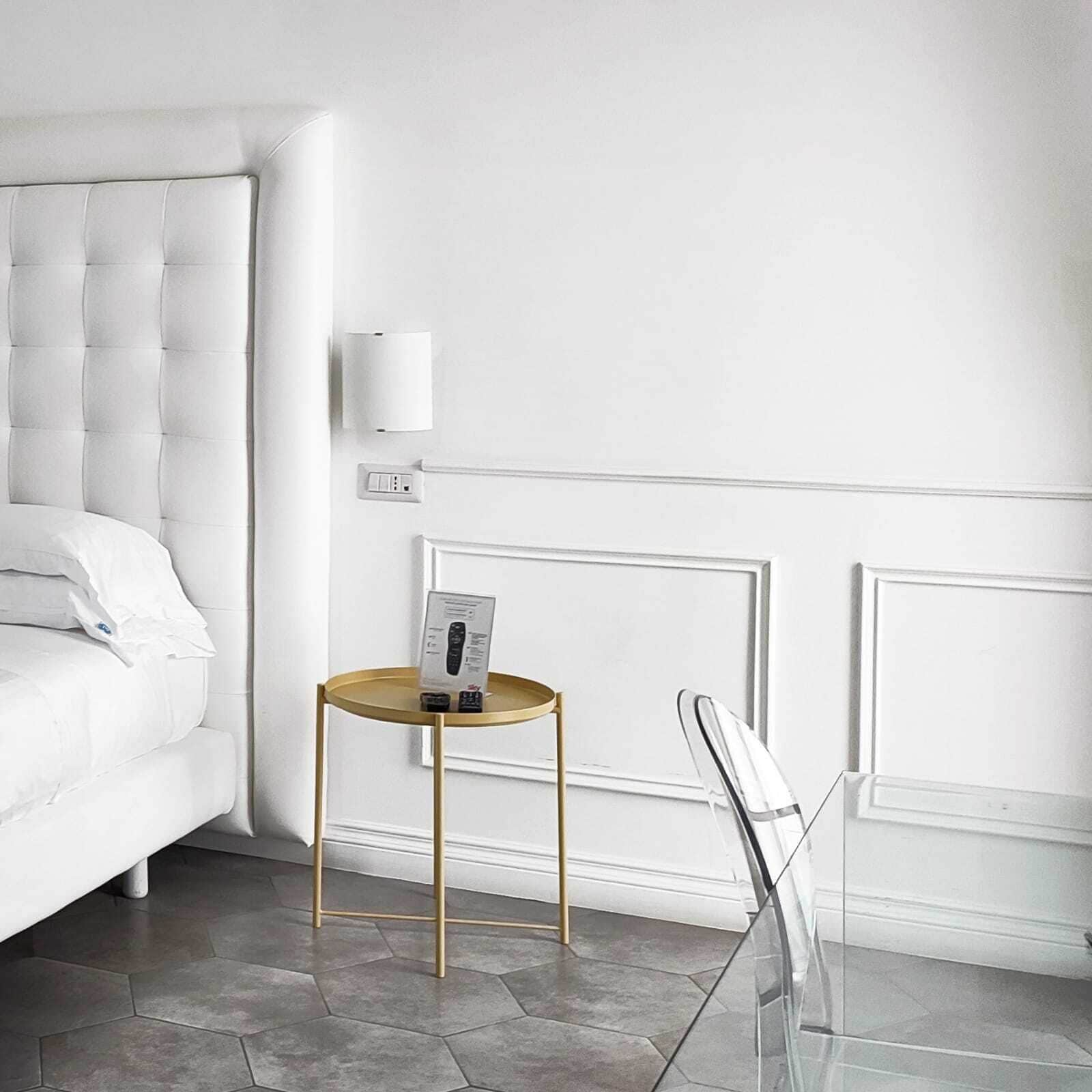 A modern bedroom with a tufted headboard, a bedside table with a remote control, and a wall-mounted light fixture.