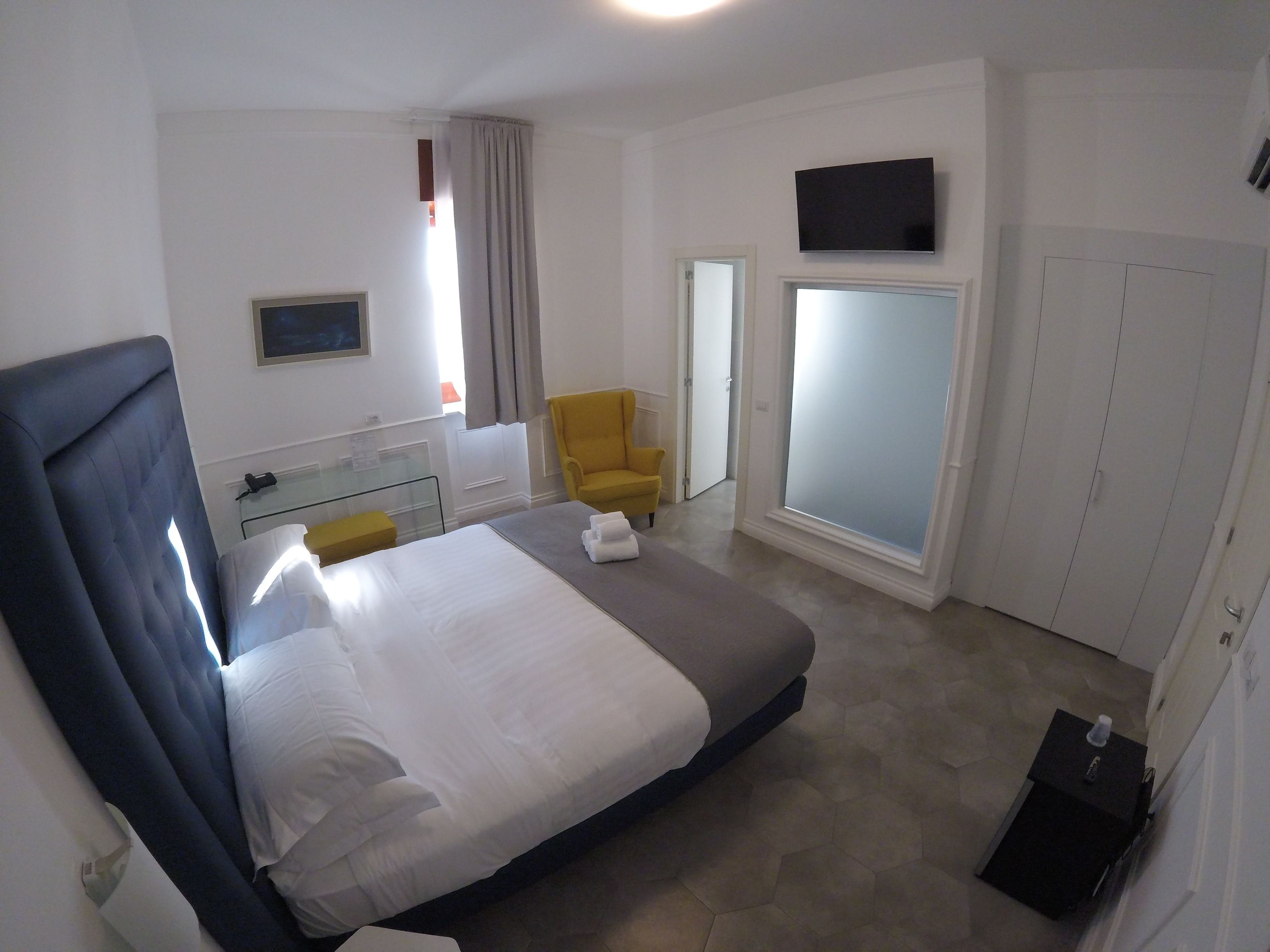 A hotel room with a large bed, a desk, a chair, a TV, and a wardrobe.