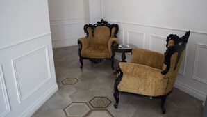 Een kamer met twee sierlijke stoelen en een klein tafeltje, witte wanden en vloertegels met een patroon.