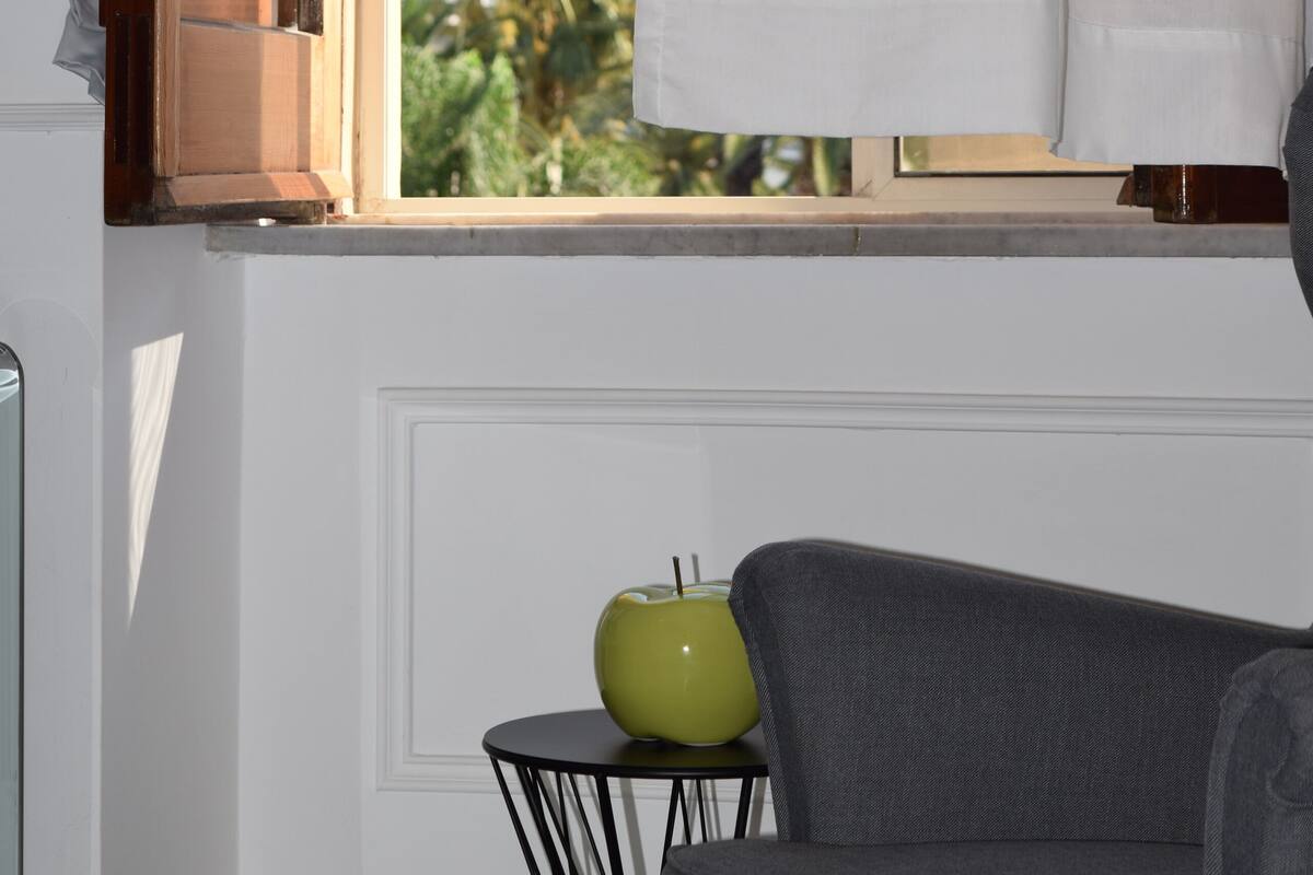 Une pièce avec une fenêtre, un bol vert posé sur une table noire et un canapé gris.