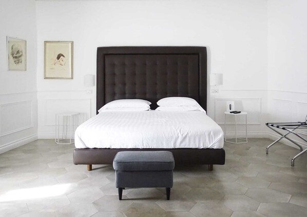 A modern bedroom with a large bed, a bedside table, a chair, and a floor lamp. - RAVIDA SUITES (Pompei)