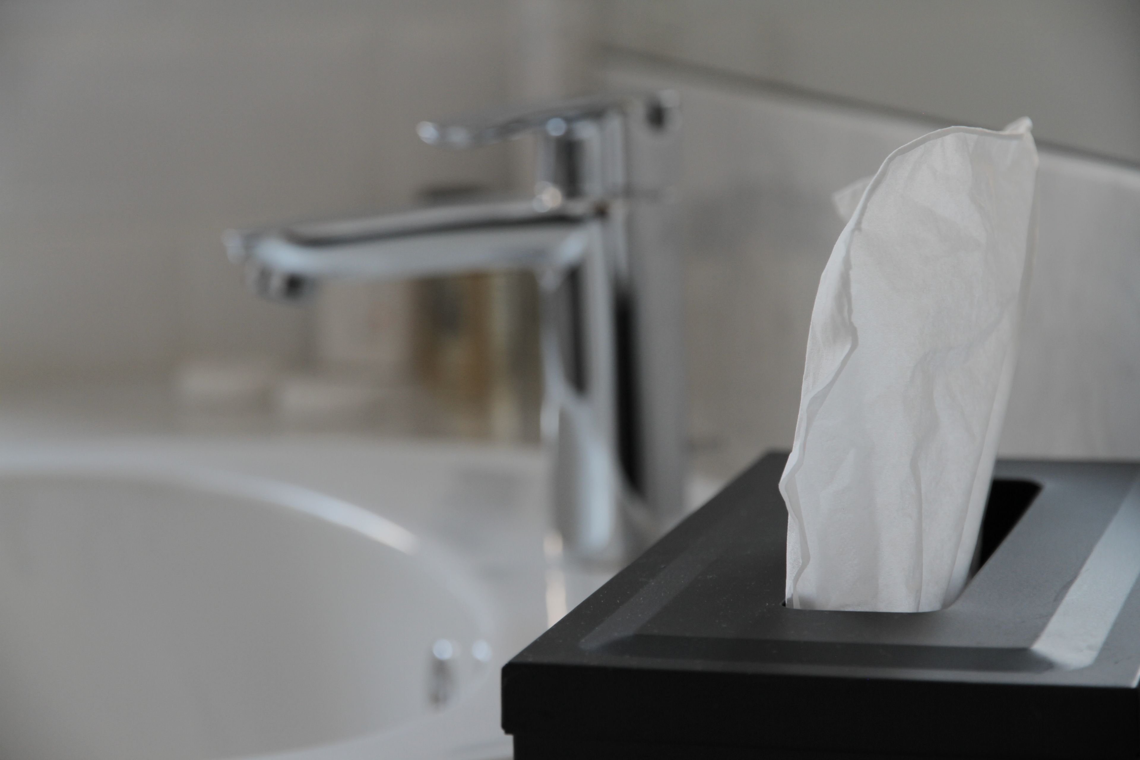 A tissue box in a bathroom with a modern faucet.