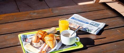 Uma mesa de piquenique com uma bandeja contendo croissants, um sanduíche, um ovo cozido, um copo de suco de laranja e uma xícara de café.