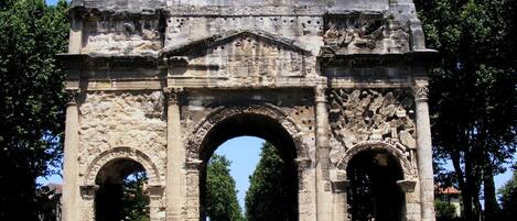 An ancient stone archway with three arches, surrounded by trees and a clear sky.