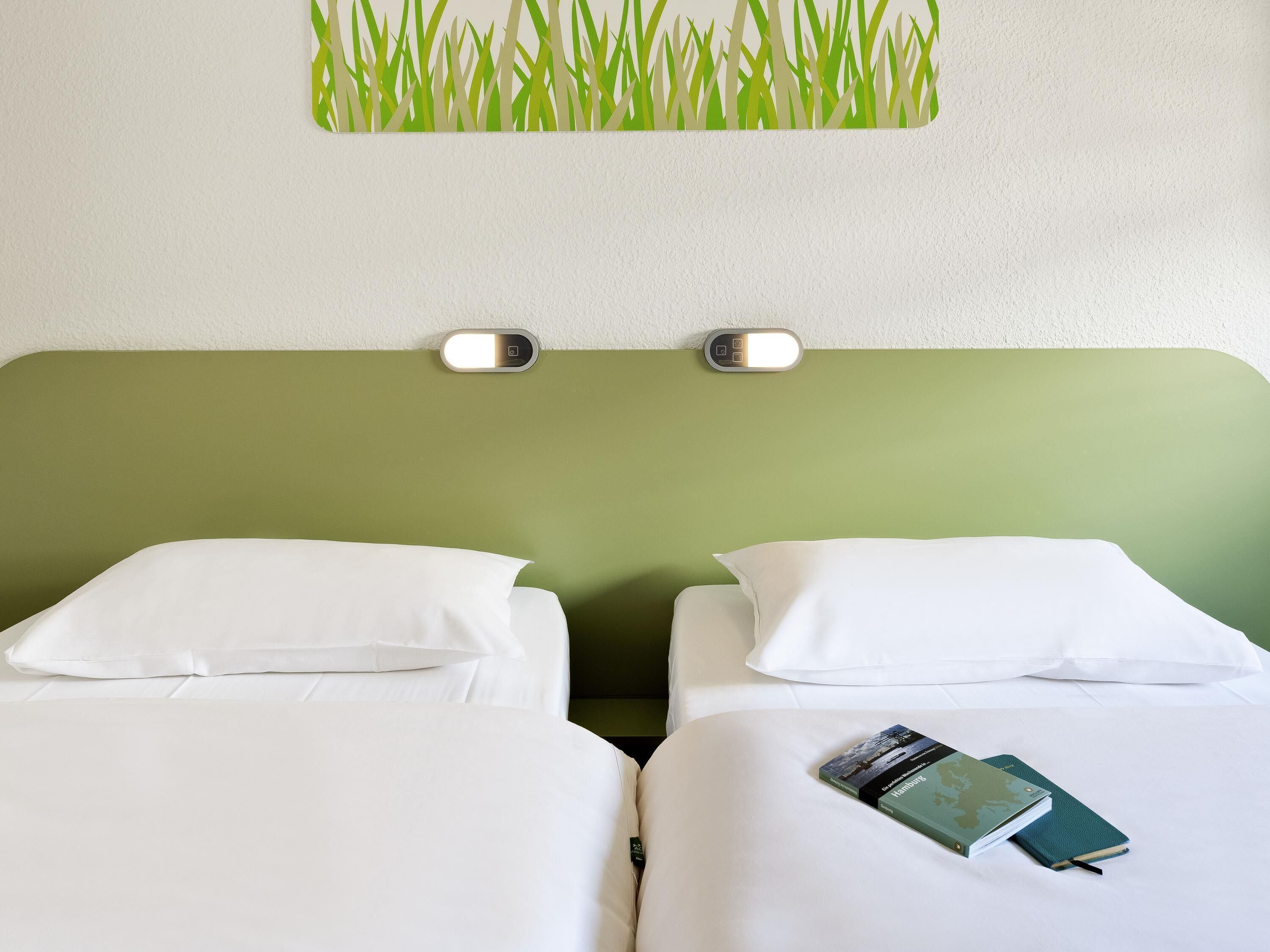 Une chambre d’hôtel avec deux lits, une tête de lit verte et un luminaire fixé au mur.