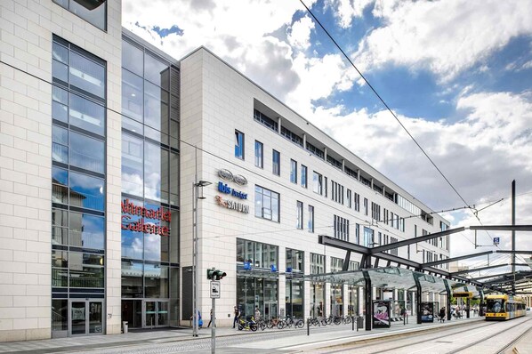 Een modern gebouw met grote ramen, een overdekte ingang en een tramlijn.