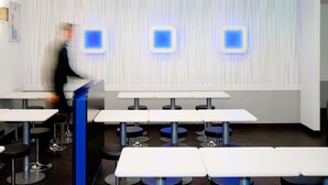 A modern restaurant with white tables and blue bar stools, a patterned wall, and a ceiling light fixture.