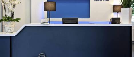 Mostrador de recepción con un fondo azul, un reloj y una planta en maceta.