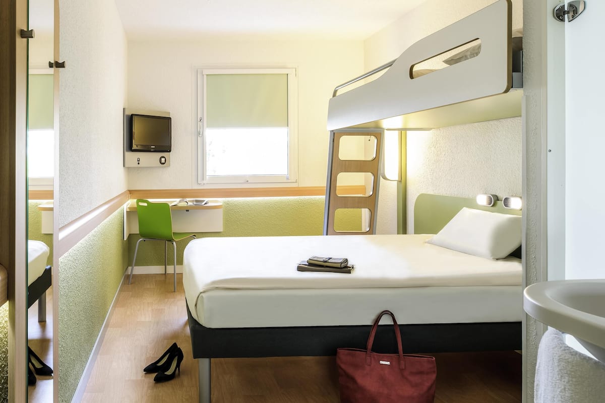 A compact hotel room with a bunk bed, a desk with a chair, a television, and a window.