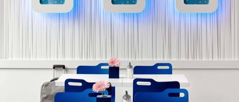 A modern dining area with a white table, blue chairs, and a decorative wall with three blue square frames.