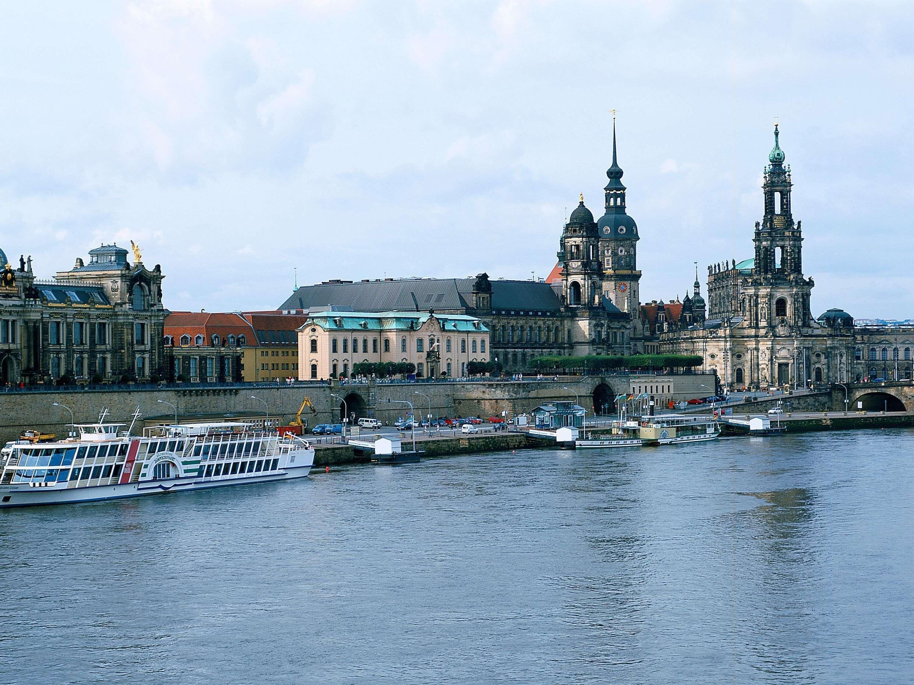 A river with a boat docked, a bridge, and historic buildings with domes and spires.