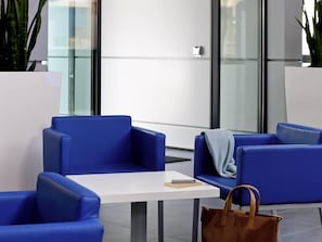 Un espace d’attente moderne avec des sièges bleus, une table blanche et un sac à main marron posé sur le sol.