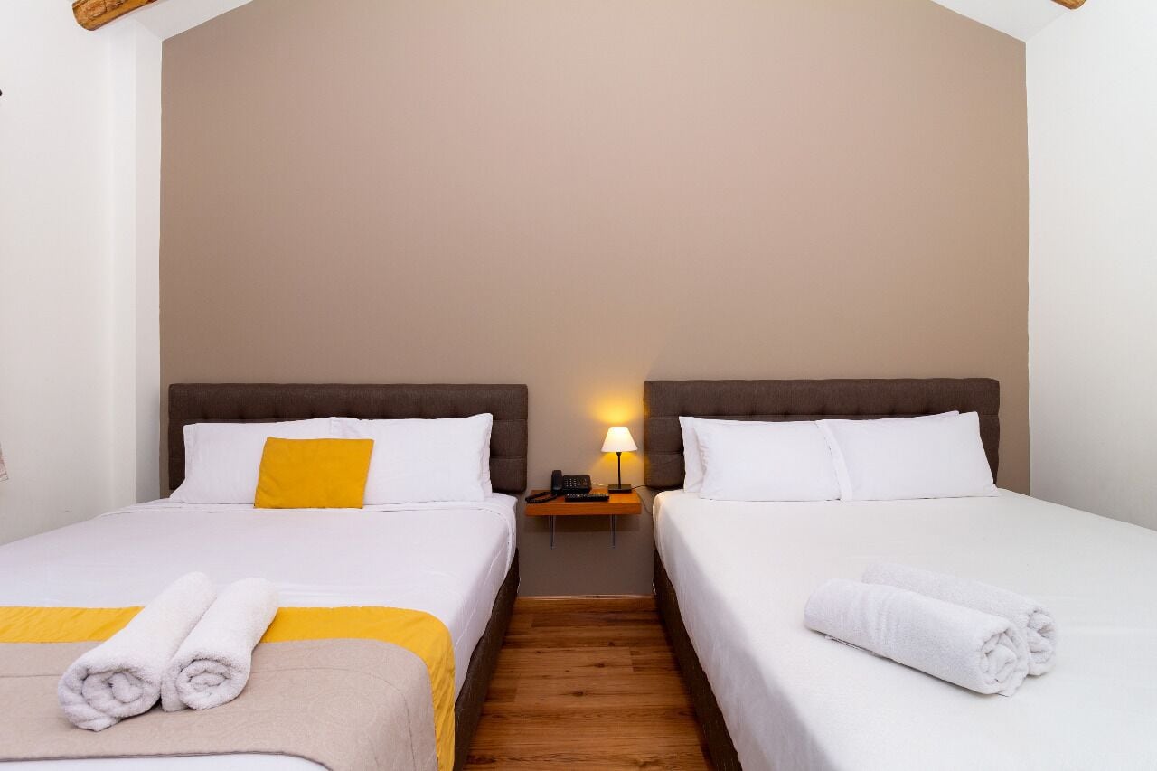 A double room with two beds, a nightstand with a lamp, and towels on the beds.