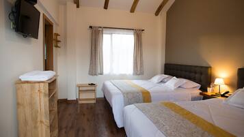 A hotel room with two beds, a wooden dresser, a television, a window with curtains, and a bedside lamp.