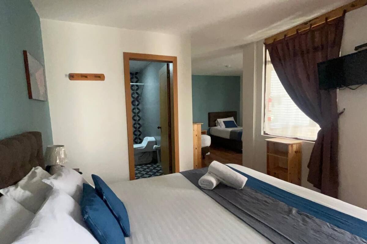 Una habitación de hotel con una cama grande, un cabecero de madera, un televisor montado en la pared y una ventana con cortinas.