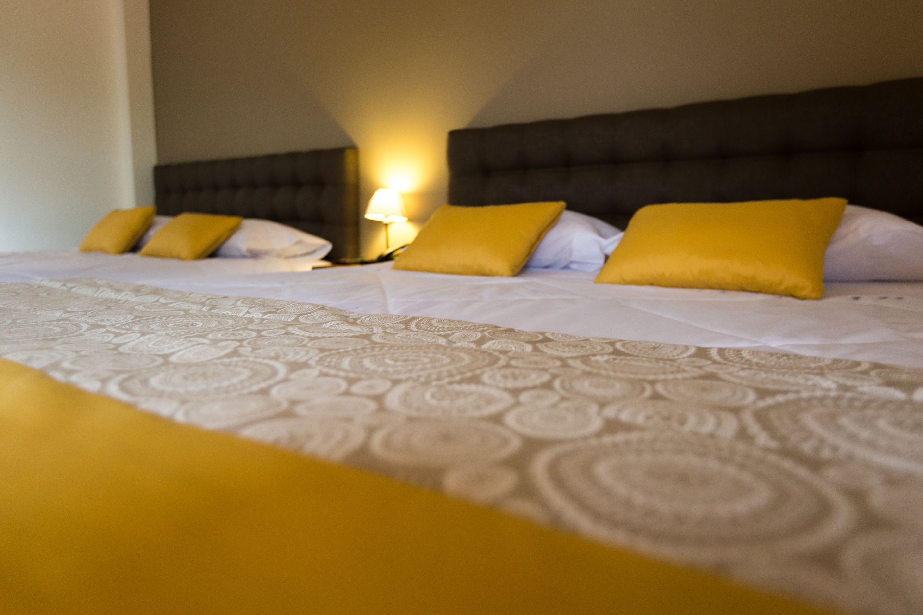 Habitación de hotel con una cama grande, varios almohadones y una lámpara de noche.