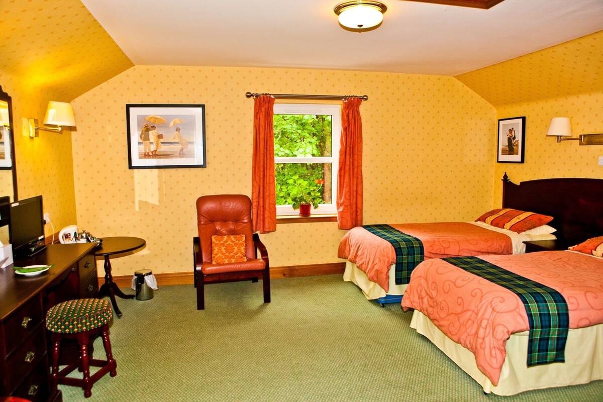 A hotel room with two beds, a desk, a chair, and a window with curtains.