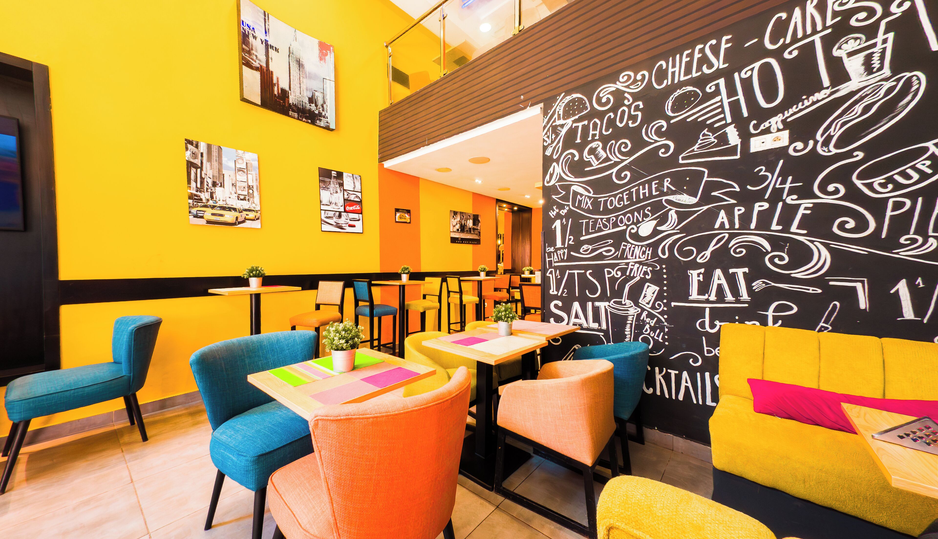 A brightly lit restaurant with yellow walls, colorful chairs, and a chalkboard menu.