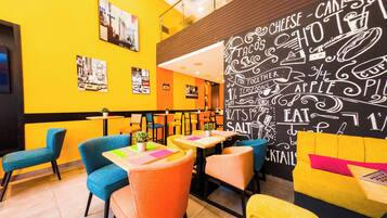 A brightly lit restaurant with yellow walls, colorful chairs, and a chalkboard menu.