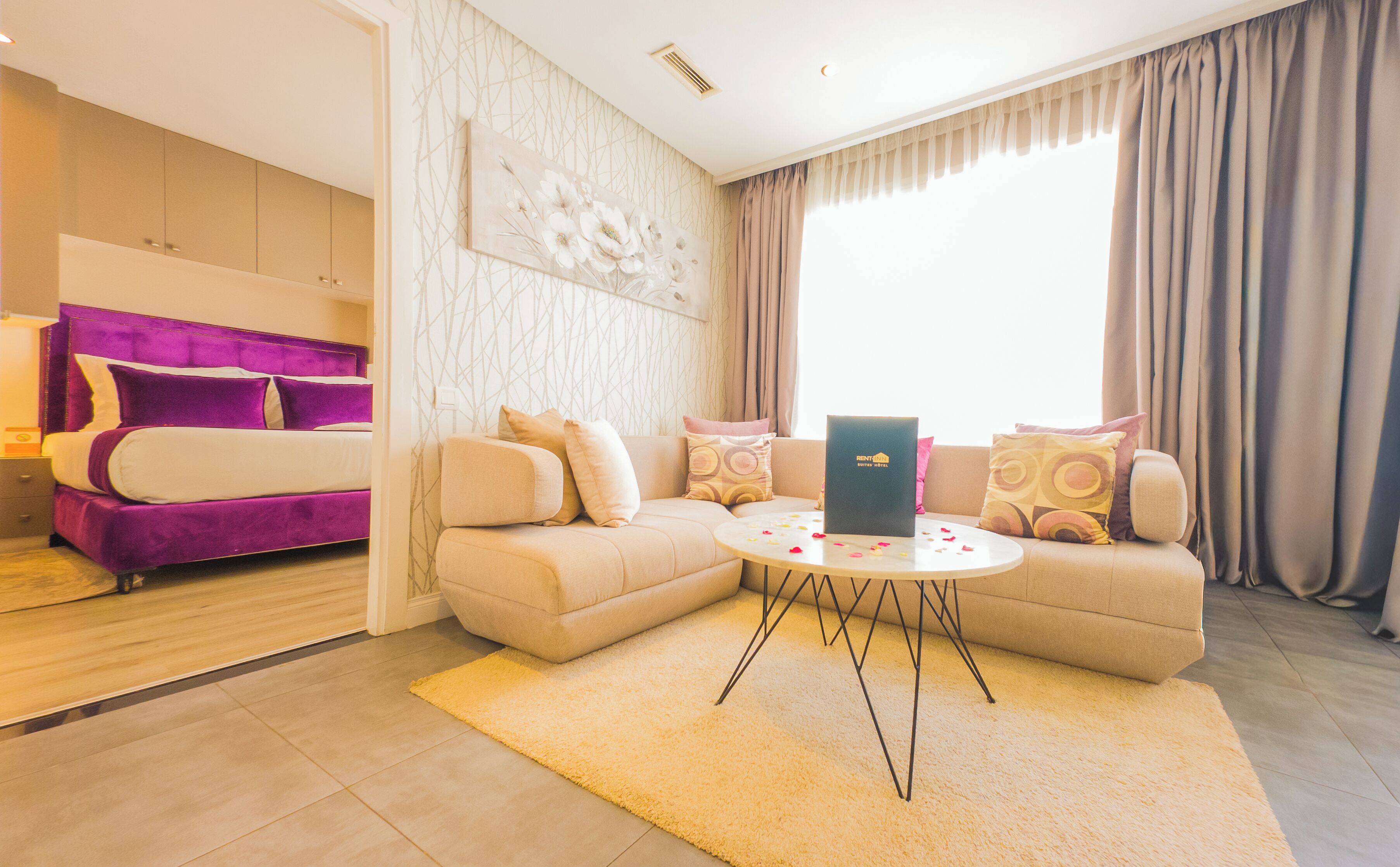 A modern hotel room with a bed, sofa, and a small table with a laptop.