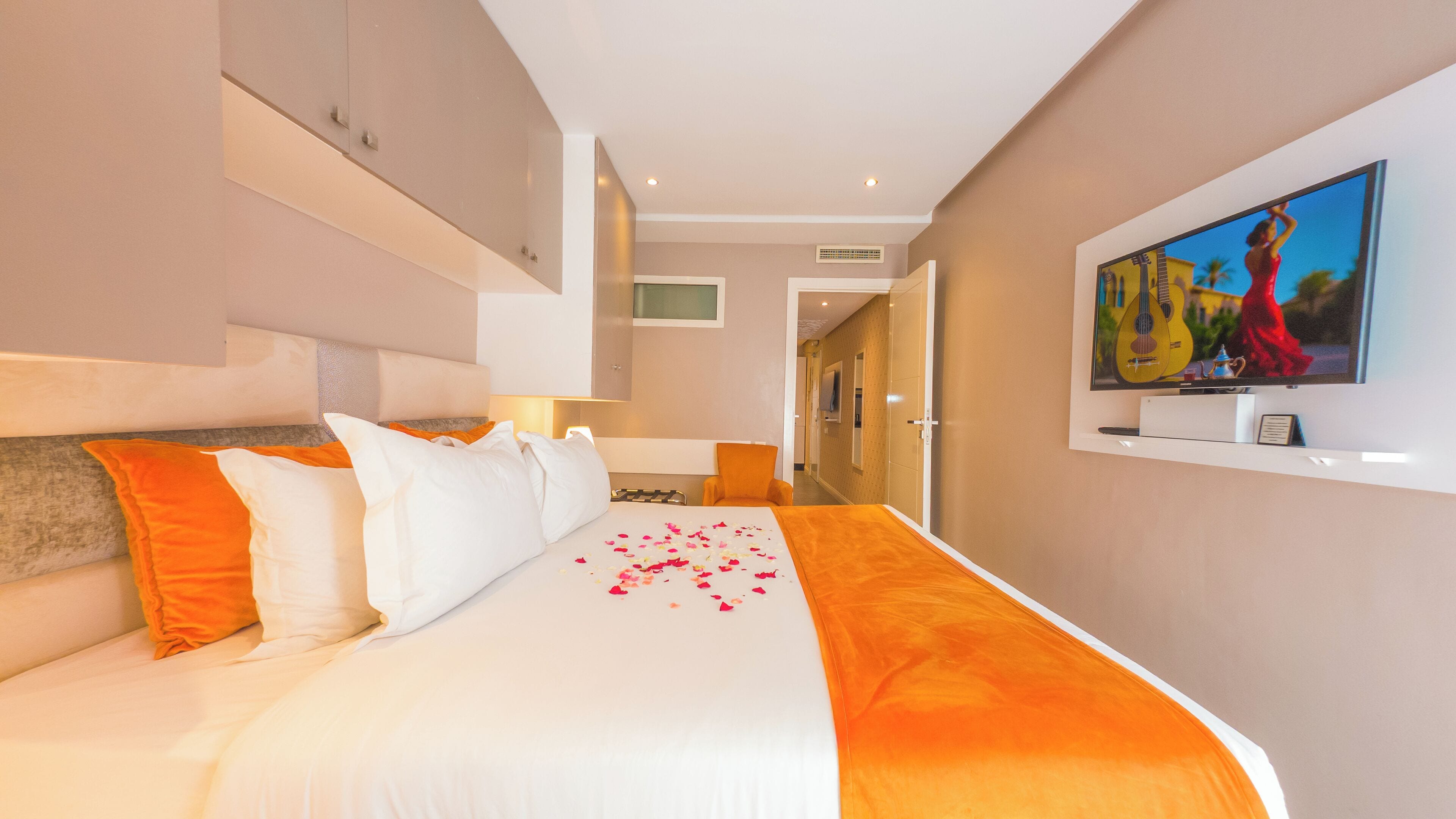 A hotel room with a large bed, a television mounted on the wall, and a hallway leading to another room.